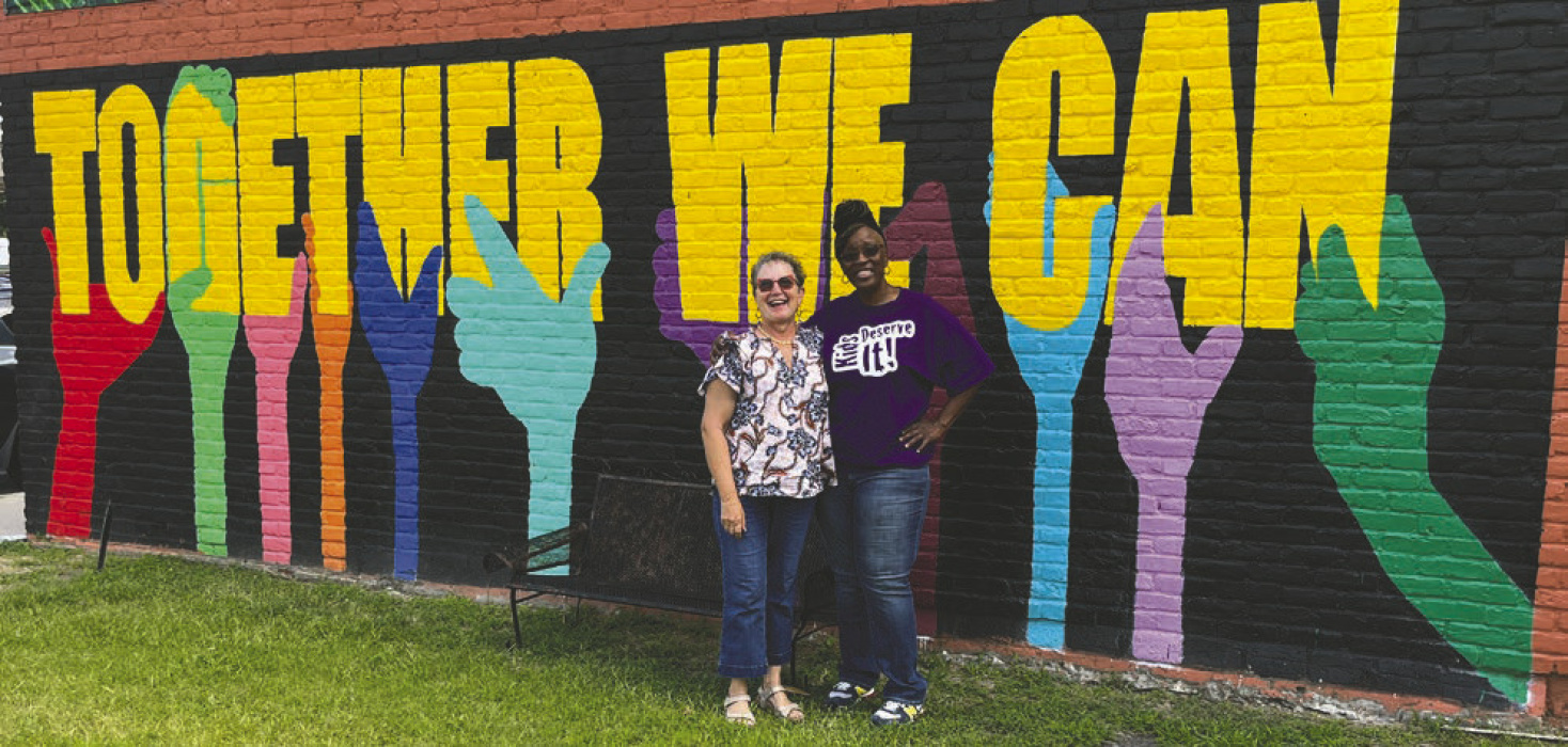 Sara Beth Howard (left) and Wanda Manning, two local artists who are part of a team seeking grant funding to bring art education to the East Carroll community, stand in front of the “Together We Can” mural in Lake Providence, designed by Brandon Virgil Sr., a former Lake Providence resident who will be part of the initiative’s education team, which also includes artist Catherine Oswalt. LAURA ARVIN